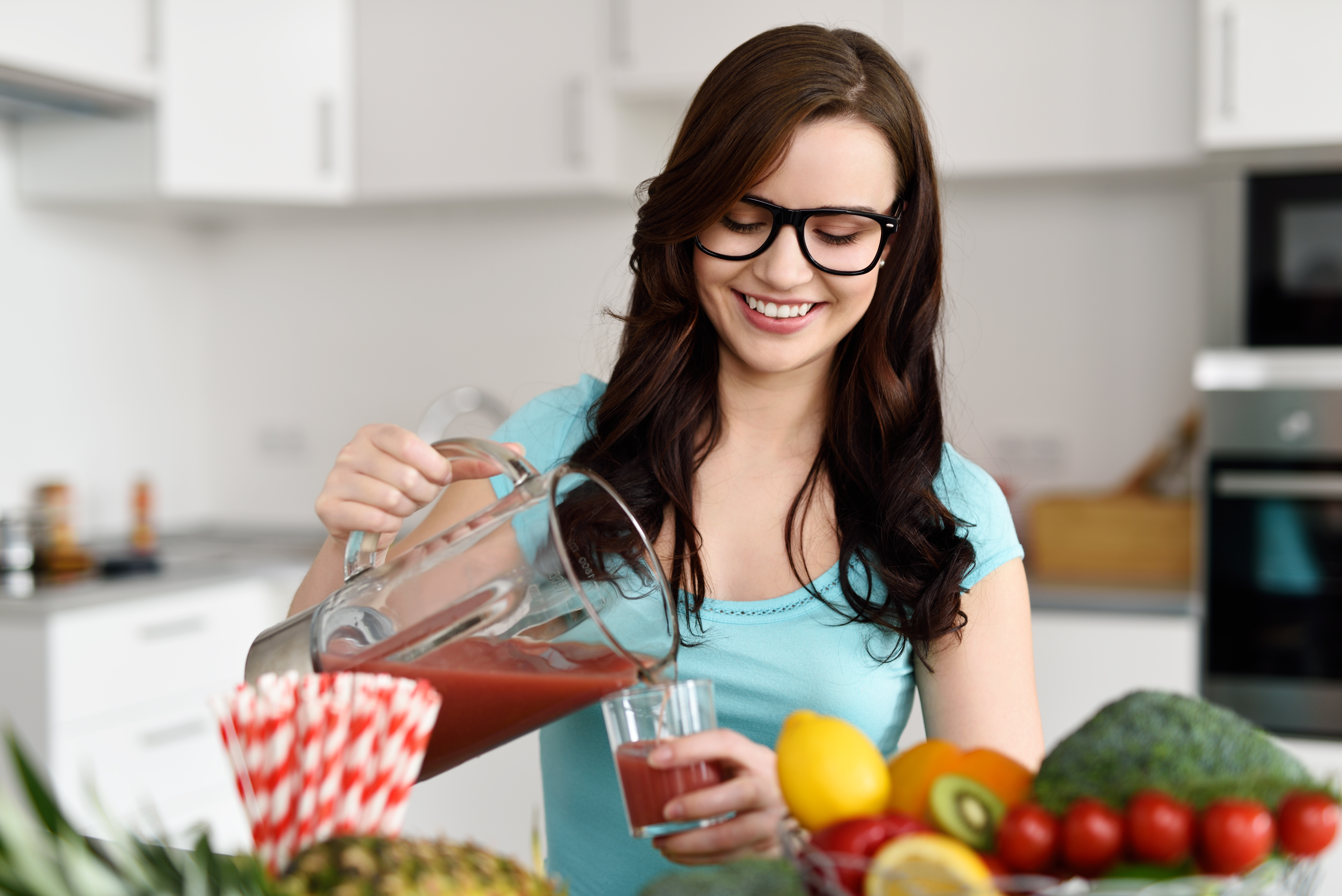 Happy healthy young woman wearing glasses pouring vegetable smoothies 